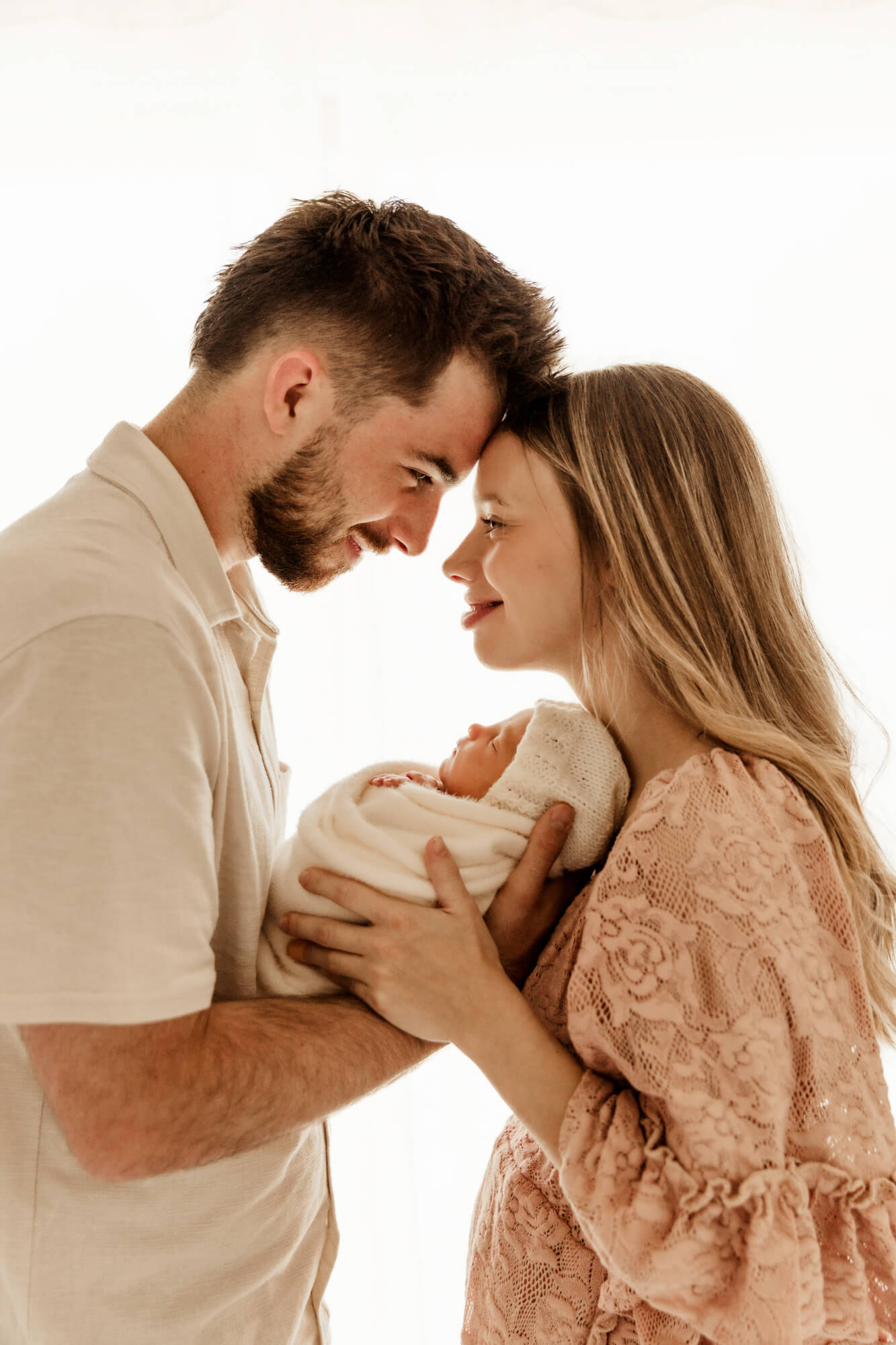Mother and father smile at one another while holding their two week old baby girl.