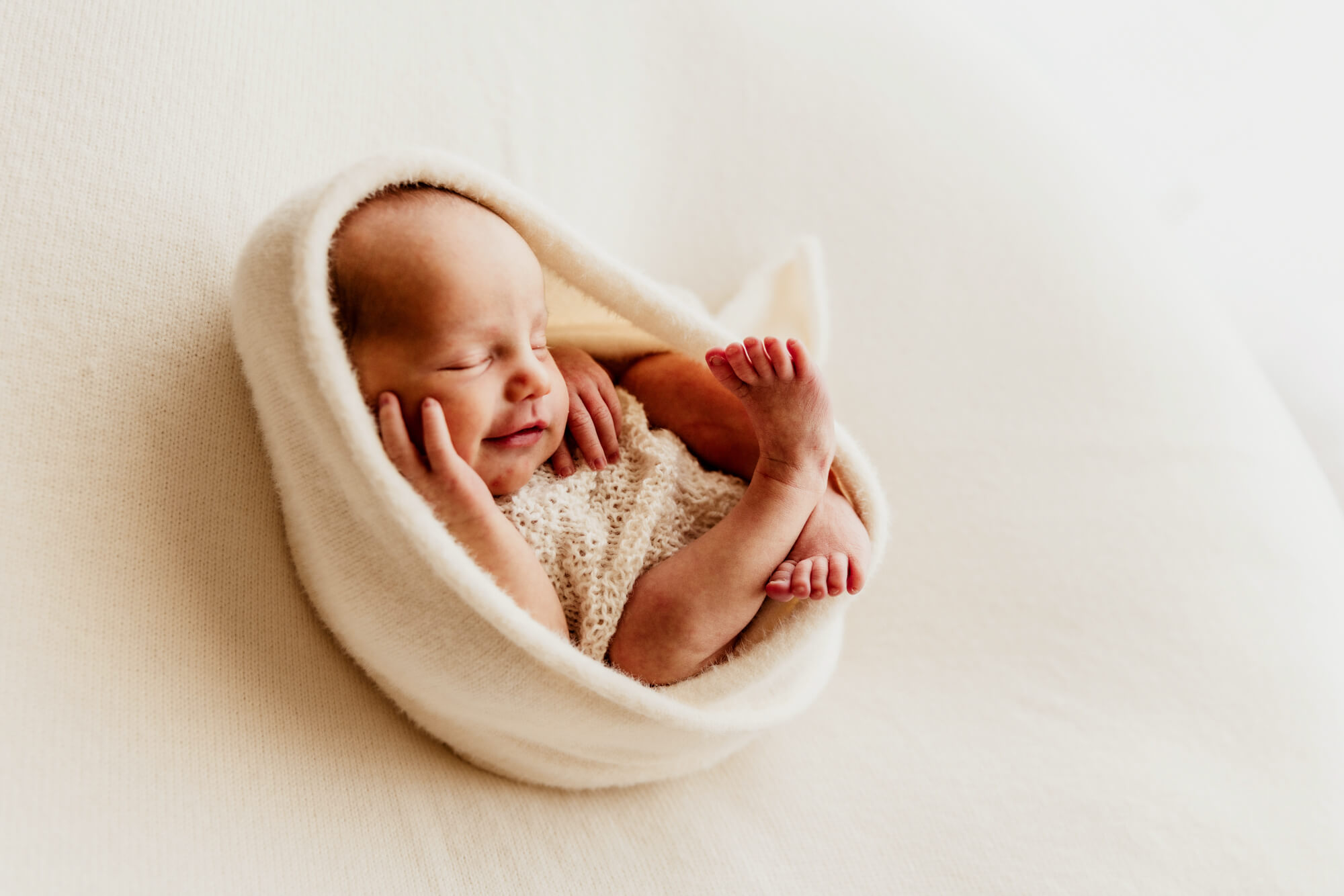 Baby girl smiles while being swaddled in a soft white wrap.