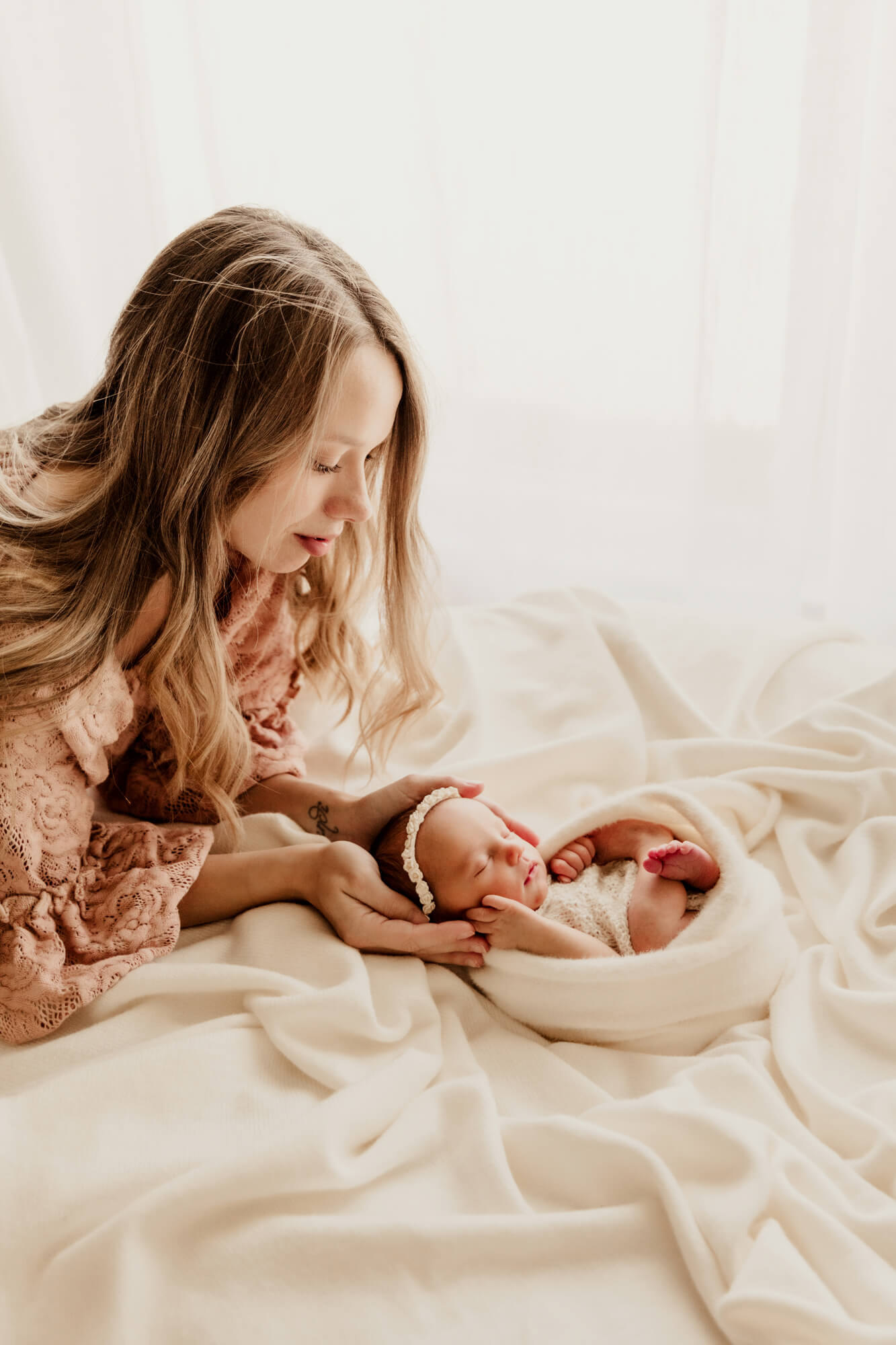 Mother tends to her newborn baby girl who is swaddled in white, postpartum doula OKC.