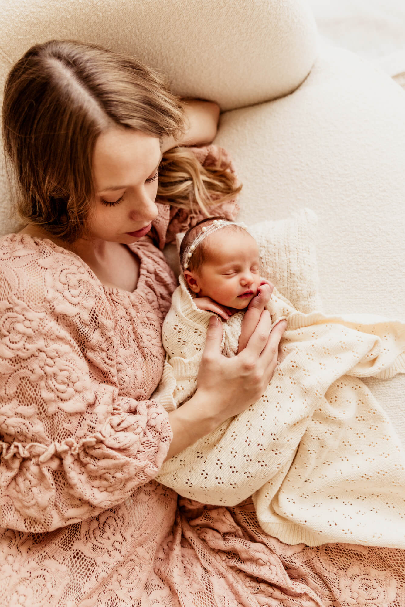 Mother wearing a pink lace dress laying next to her newborn baby girl wrapped in a blanket, postpartum doula OKC.