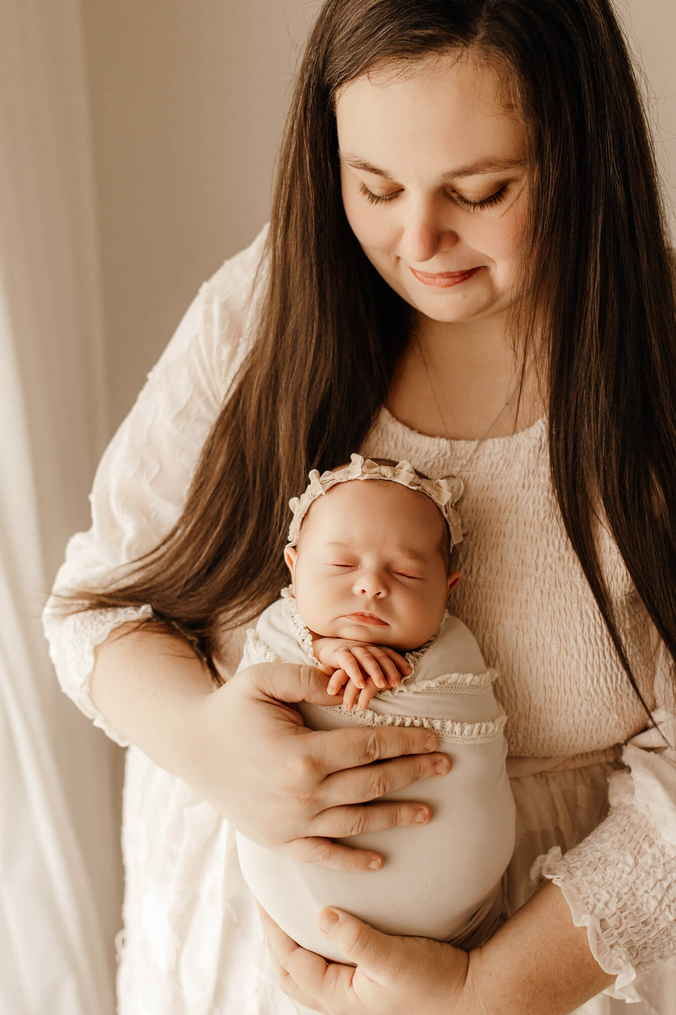 A happy new mom cradles her sleeping newborn against her chest while standing in a window after visiting Oklahoma Mother's Milk Bank