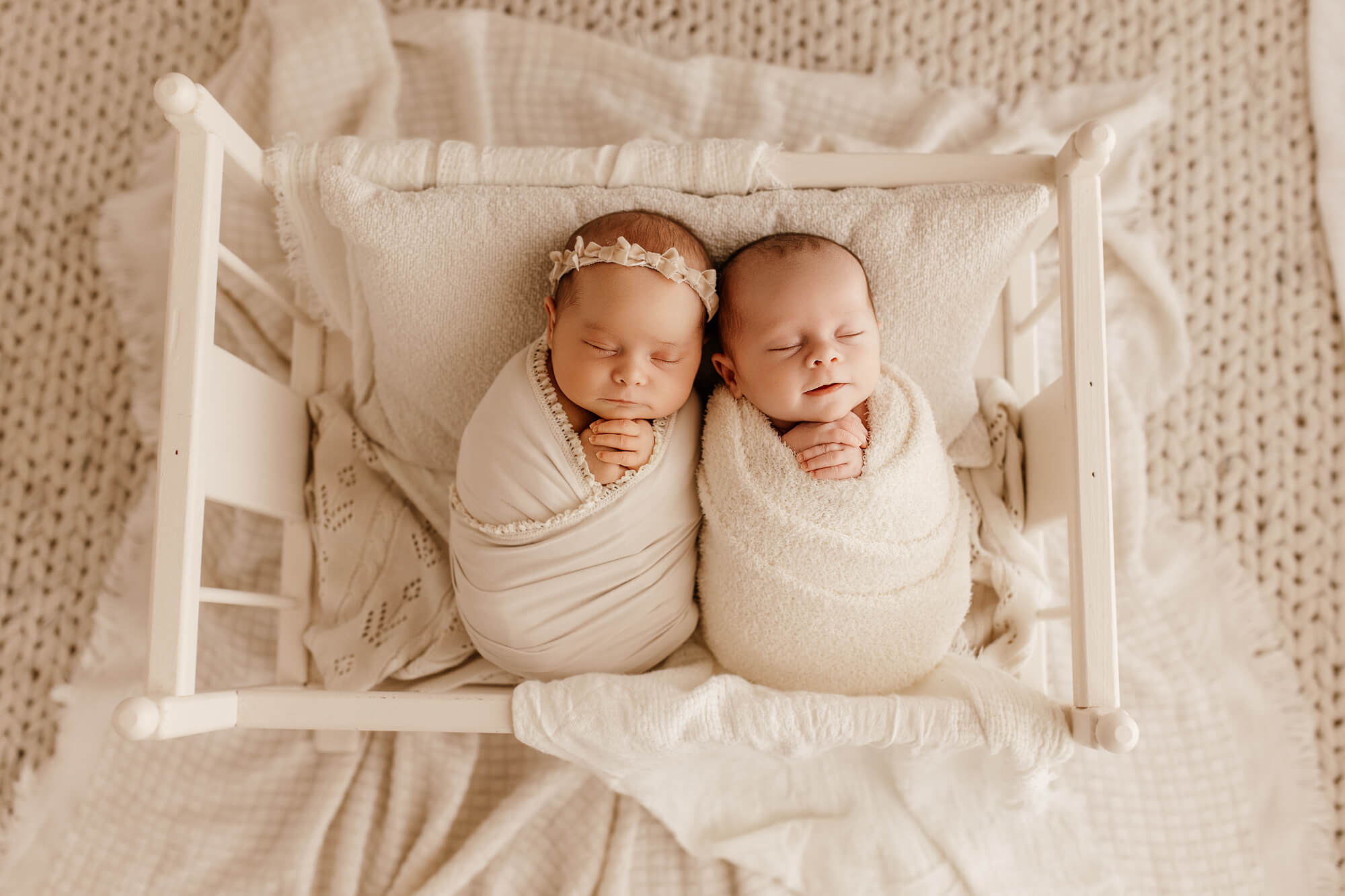 Twin newborn brother and sister sleep in a tiny crib against each other in white swaddles after visiting Oklahoma Mother’s Milk Bank