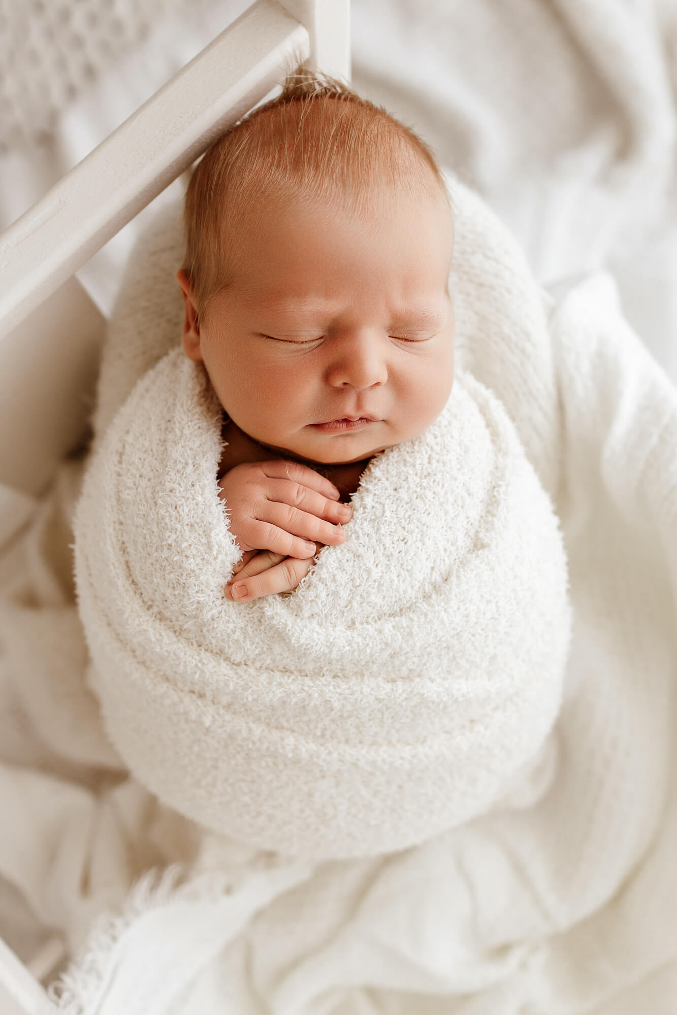 A newborn baby sleeps in a white swaddle with hands poking out after meeting a sleep coach in OKC